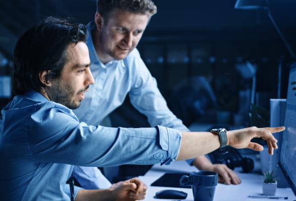 Two corporate traders sit in front of a desktop computer to analyse the StoneX Pro solutions.